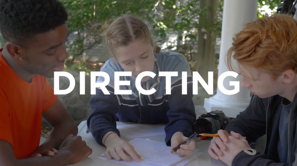 Photo of three students seated together, looking at pages of a script with the word 'DIRECTING' overlaid in white text